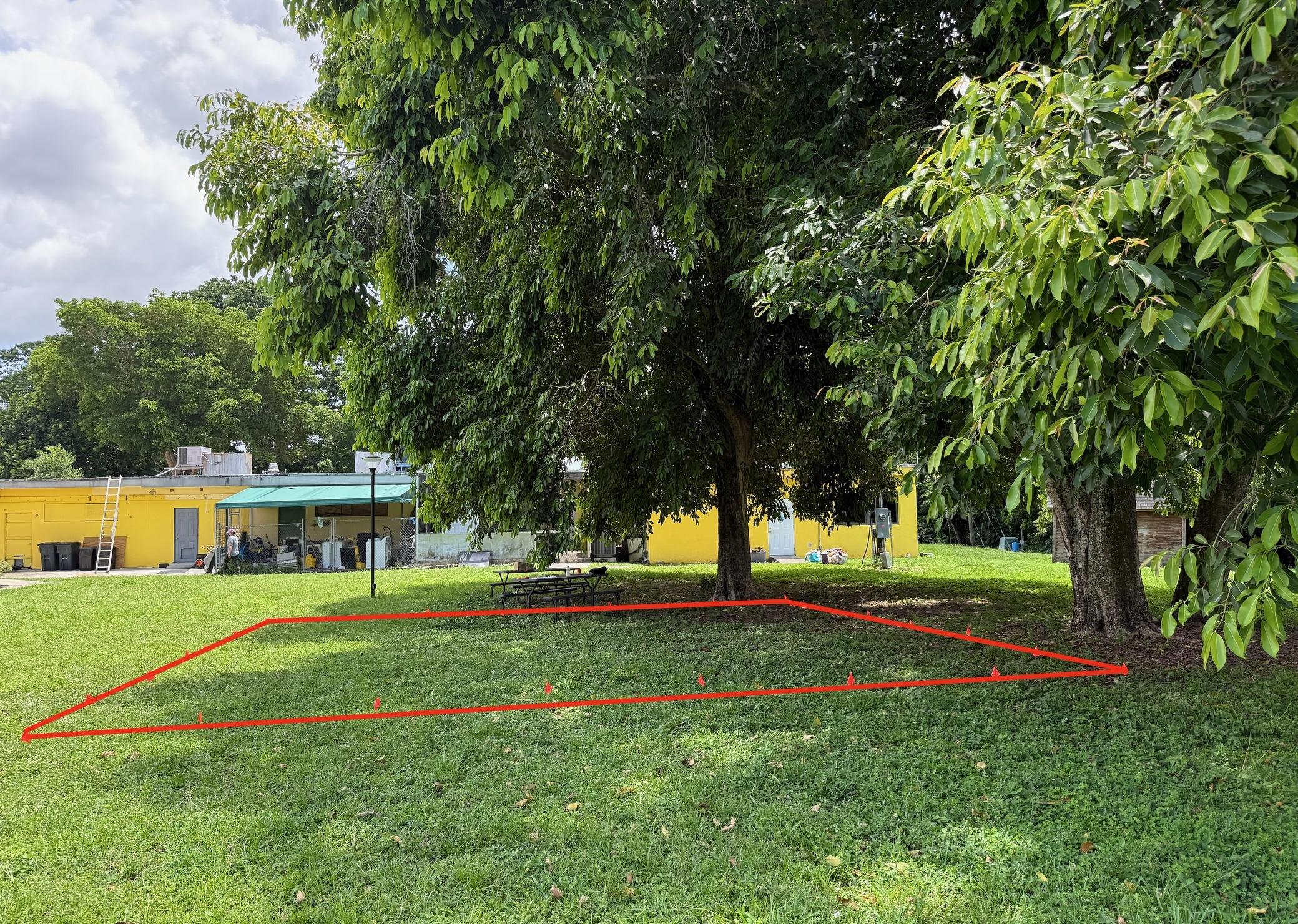 Existing grassy project site beneath trees, with the proposed area outlined in red